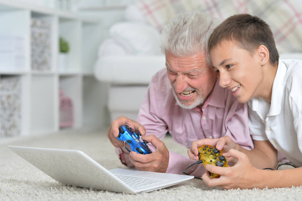 grandfather and grandson lying on floor and playing computer games on laptop - Foto, imagen