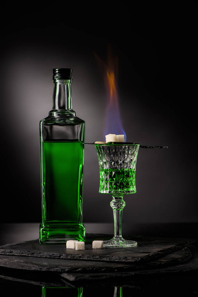 Nahaufnahme eines Löffels mit Zuckerwürfeln über brennendem Absinth im Glas auf dunklem Hintergrund - Foto, Bild