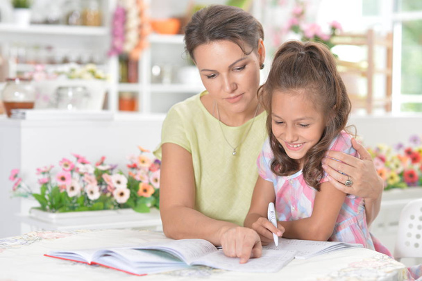 Cute little girl with her mother doing homework together in kitchen - Zdjęcie, obraz