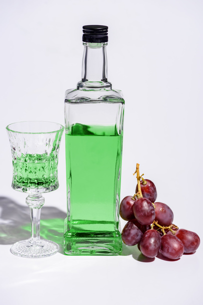 cristal y botella de absenta con rama de uva sobre blanco
 - Foto, Imagen