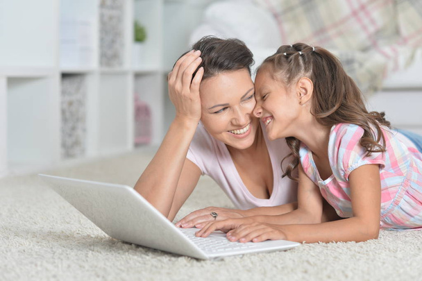 boldog anya és lánya együtt használják a laptop otthon a földön fekve - Fotó, kép