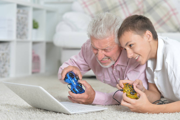 grandfather and grandson lying on floor and playing computer games on laptop - Photo, Image