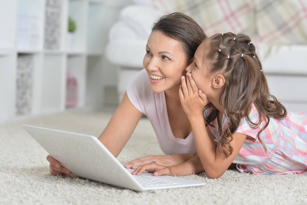 happy mother and daughter using laptop together while lying on floor at home - Photo, Image