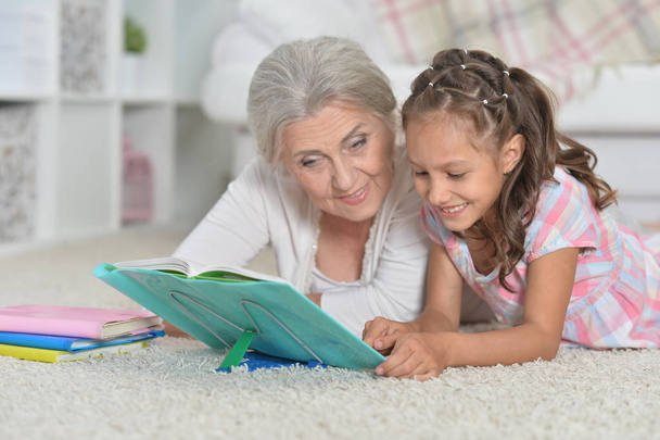 Grandmother with cute little girl doing homework together while lying on floor - Foto, Imagen