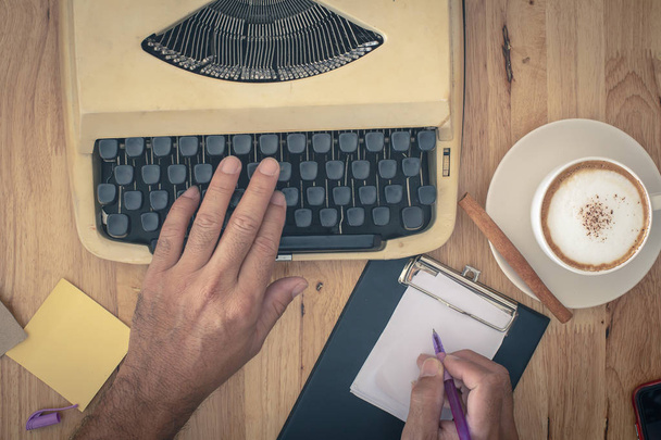 Mies käyttää vintage kirjoituskone ja kuppi kahvia puinen pöytä
 - Valokuva, kuva