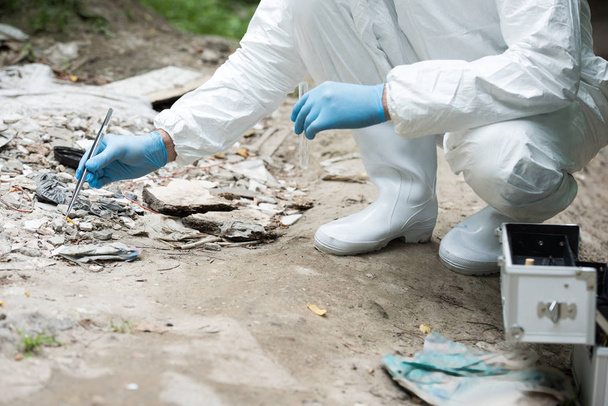 cropped image of male scientist in latex gloves taking sample of stone by tweezers outdoors - Foto, imagen