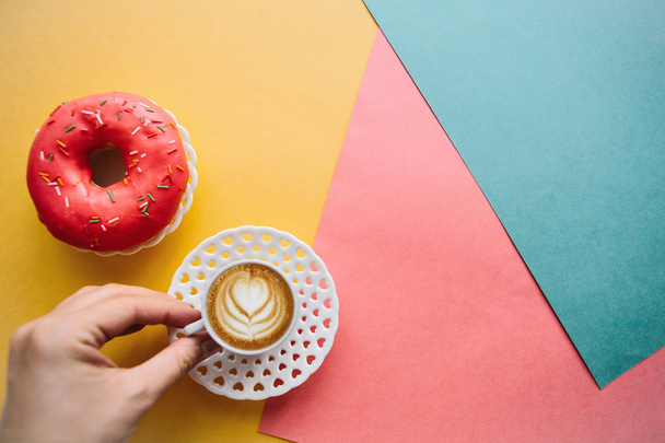 Το κορίτσι πρόκειται να πιείτε τον καφέ και να φάτε τα ντόνατ που βρίσκονται στην επιφάνεια του χρώματος - Φωτογραφία, εικόνα