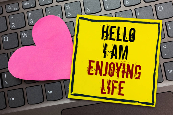 Handwriting text writing Hello I Am Enjoying Life. Concept meaning Happy relaxed lifestyle Enjoy simple things Written on black bordered yellow page touched pink heart on computer keyboard - Photo, Image