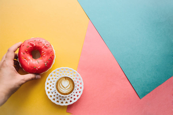 The girl is going to drink coffee and eat donut which lie on the colored surface - Photo, Image