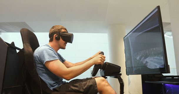 Вид сбоку сидя и играя в гоночный симулятор в гарнитуре виртуальной реальности
  - Фото, изображение