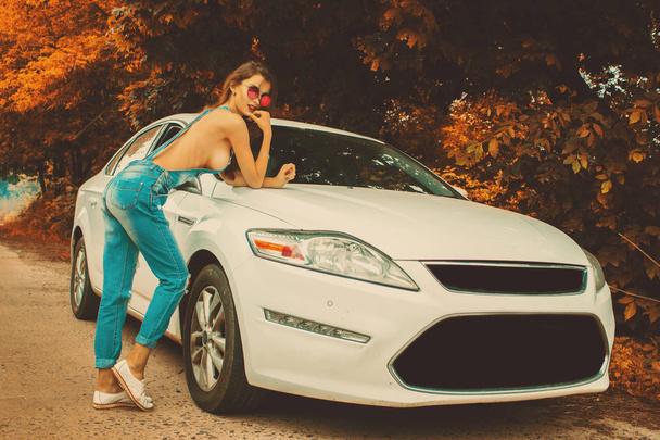 Seksowna brunetka piękna w dżinsy ogólnej w pobliżu biały samochód w czasie jesieni - Zdjęcie, obraz
