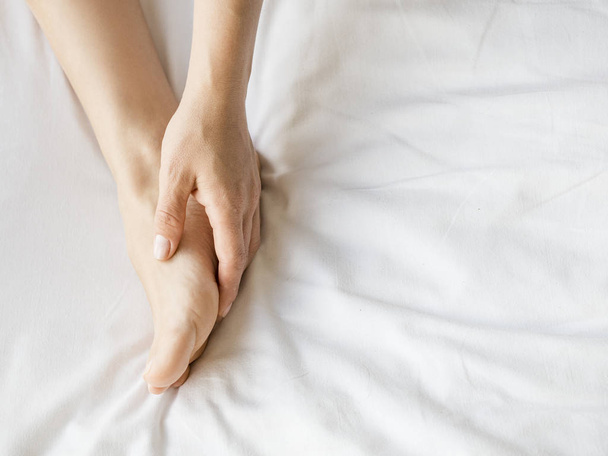 Young woman massaging her foot on the bed. Skincare concept - Photo, Image