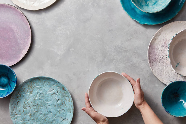 colorful porcelain pottery bowls on stone gray background, female hands holding handmade bowl  - Zdjęcie, obraz