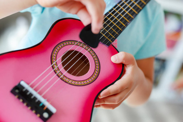 Közeli kis aranyos szőke lány otthon kis ukulele gitározni a tanulás, a szórakozás. Kisgyermek lány próbál játszani játék hangszer beltéri - Fotó, kép