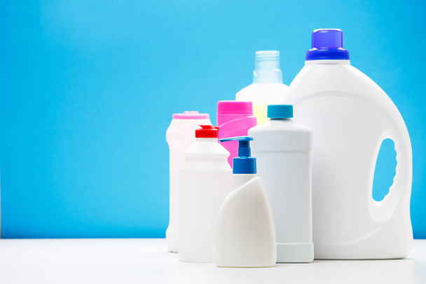 Photo of several bottles of cleaning products on white table isolated on blue background, place for inscription - Foto, immagini