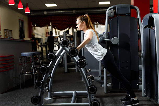 schlanke Frau stützt sich in einem Fitnessstudio auf einen Hantelständer - Foto, Bild