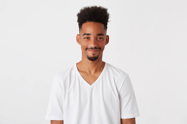 Portrait of smiling attractive african american young man with afro hairstyle wears t shirt feels happy and relaxed isolated over white background Looks directly in camera - Fotografie, Obrázek