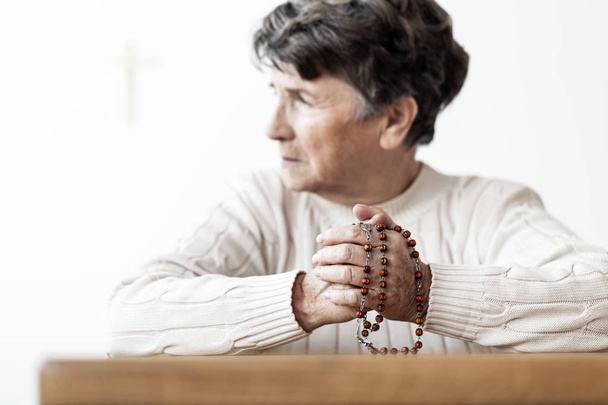 Senior woman holding rosary while praying in the church. Focus on hands - Foto, imagen