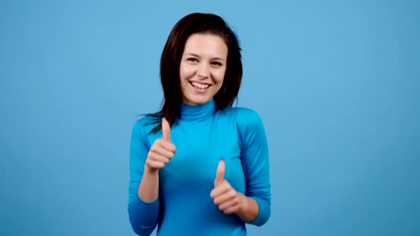 Positive joyful cheerful woman showing thumbs up on blue background - Filmati, video