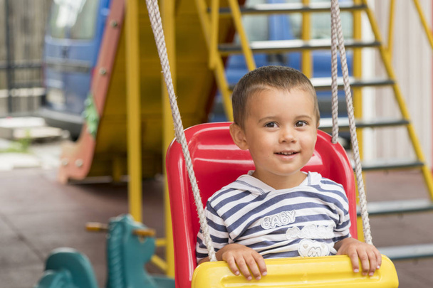 Bambino 2 anni in sella ad un'altalena. Bambino felice nel parco giochi
. - Foto, immagini