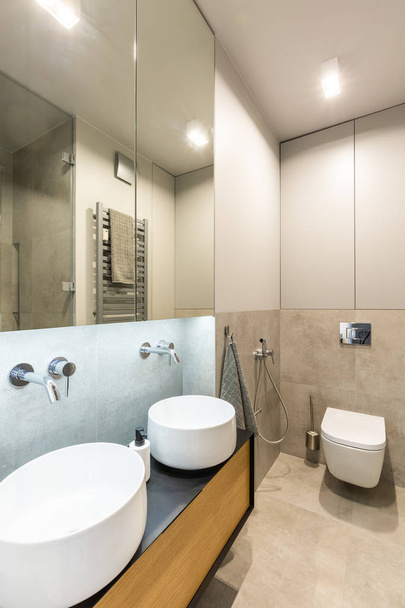 Mirror above white washbasins in beige bathroom interior with light and toilet. Real photo - Fotoğraf, Görsel