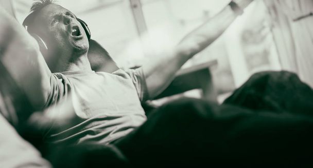 A man celebrating a goal while listening to his favourite team on wireless headphones in a relaxing armchair. Styling and grain effect added to image. - Photo, Image