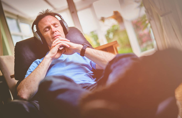 Un hombre relajado escuchando música en auriculares inalámbricos en una silla cómoda
 - Foto, Imagen