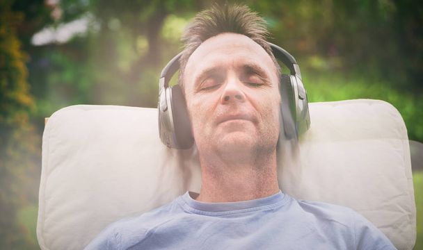 Ένας άντρας απολαμβάνει να ακούτε μουσική σε ασύρματα ακουστικά σε μια πολυθρόνα χαλάρωσης. Επίδραση styling και κόκκους προστεθεί στην εικόνα. - Φωτογραφία, εικόνα