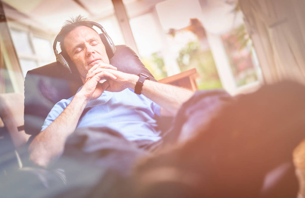 Człowieka, ciesząc się, słuchając muzyki na bezprzewodowe słuchawki w fotel relaksacyjny. Stylizacja i ziarna efekt dodane do obrazu. - Zdjęcie, obraz