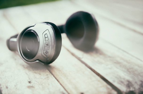 A 45 degree view of a set of wireless headphones lying on a rustic wooden table outside. Styling and grain effect added to image. - Photo, Image
