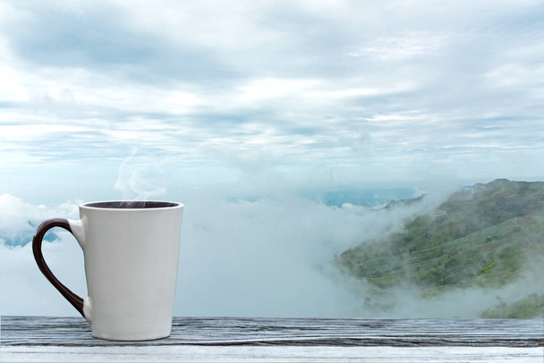 Cup coffee and tea with steam on wood table over mountains city landscape with mist sunlight winter.   Beauty nature background. Lifestyle Concept - Photo, image