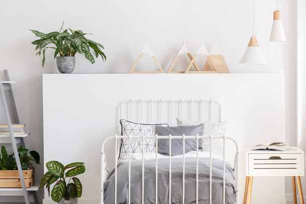Plant and triangles on headboard in teenager's bedroom interior with grey sheets on bed. Real photo - Fotó, kép