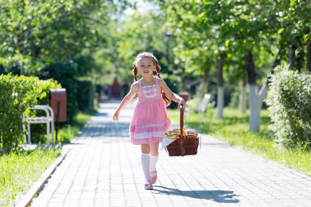 A little girl runs along the street in the city with bread and baking. The girl runs along the road with a basket of bread. - Фото, изображение