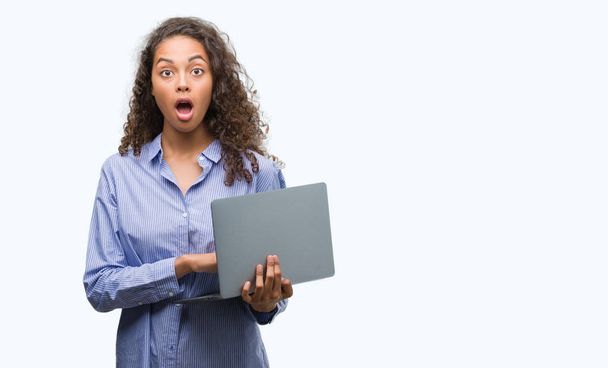 Giovane donna ispanica in possesso di computer portatile spaventato in stato di shock con una faccia a sorpresa, spaventato ed eccitato con espressione di paura
 - Foto, immagini