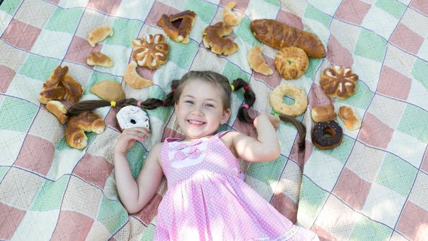 Around the head of a beautiful girl laid out a lot of bread and baking. The girl lies on a plaid among the products of bread. - Photo, image