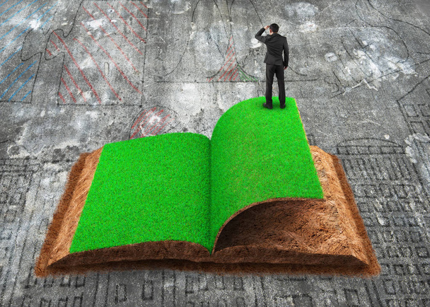 Pieni liikemies seisoo avattu kirja vihreää ruohoa ja maaperän kuvioitu, likainen doodles betonilattia tausta, käsite ECO, uusiutuvan energian ja kiertotalouden
. - Valokuva, kuva