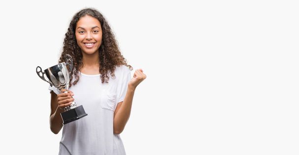 Young hispanic woman holding trophy screaming proud and celebrating victory and success very excited, cheering emotion - Fotó, kép