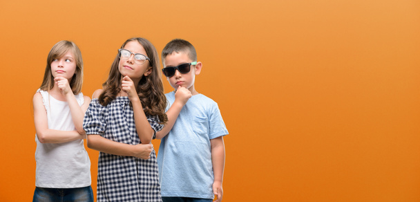 Група дітей-хлопчиків та дівчат на помаранчевому тлі серйозно думає про питання, дуже заплутана ідея
 - Фото, зображення