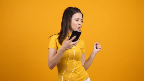 Happy young woman listening music in earphones through her smartphone - Materiał filmowy, wideo