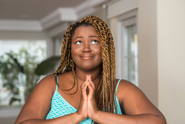 Αφρικανική αμερικανική γυναίκα στο σπίτι επαιτεία και προσεύχεται με τα χέρια μαζί με ελπίδα έκφραση προσώπου πολύ συναισθηματική και ανησυχούν. Ζητώντας συγχώρεση. Έννοια της θρησκείας. - Φωτογραφία, εικόνα