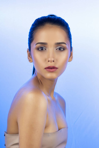 Close up portrait of a brunette girl with nude make-up and naked shoulders on white blue gradient background. Copy space. Advertising, fashion and commercial design. - Foto, immagini