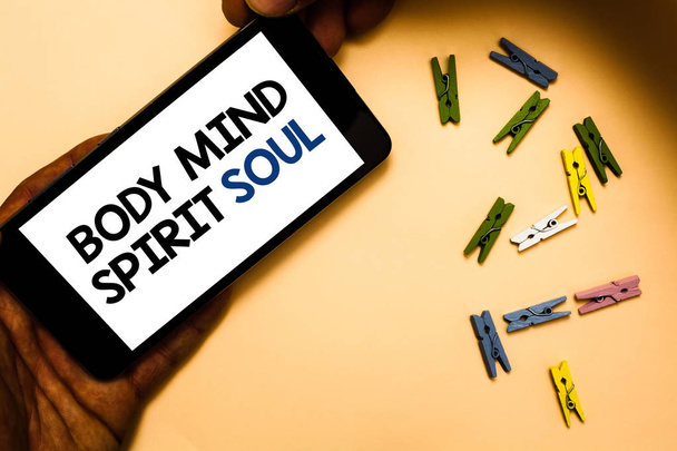 Εννοιολογική χέρι γραφή δείχνει Body Mind Soul πνεύμα. Επαγγελματίες φωτογραφία κείμενο προσωπική ισορροπία θεραπεία συνείδηση κατάσταση του νου χέρι εκμετάλλευση iphone με επιστολές και συνδετήρα χρώμα ροδακινί έδαφος - Φωτογραφία, εικόνα