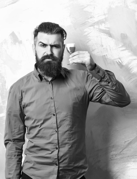 Brutal caucasian serious hipster with moustache in brown shirt holding alcoholic red shot on colorful texture background. - 写真・画像