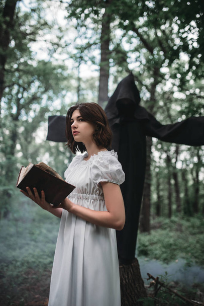 Vittima femminile e morte con cappuccio nero e falce, foresta sullo sfondo. Foto in stile horror, esorcismo
 - Foto, immagini