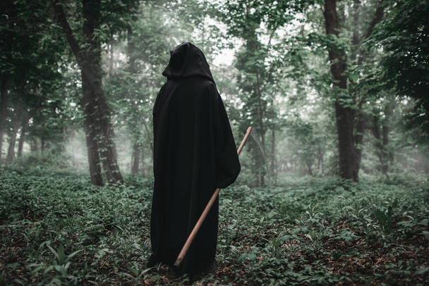Death in a black hoodie and with a scythe in the dark misty forest. Horror style, fear, spooky demon - Photo, Image