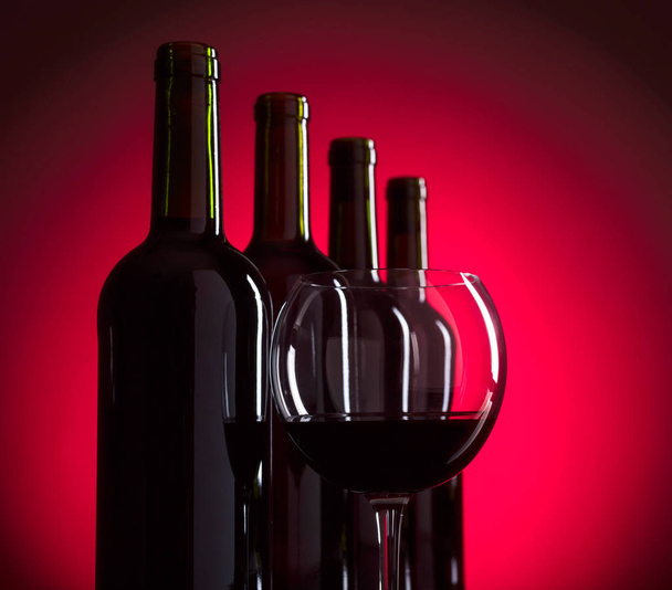 Glazen en flessen rode wijn op rode achtergrond, kopie ruimte voor uw tekst. - Foto, afbeelding