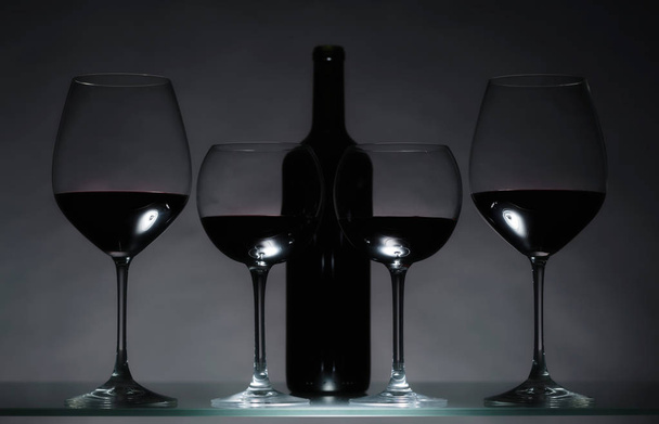 Gläser und Flasche Rotwein auf dunklem Hintergrund. - Foto, Bild