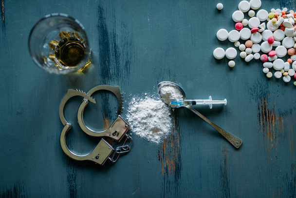 Drug user kit, narcotics concept, addiction problem. Pills are laid out on wooden table, syringe for dose, alcohol and handcuffs - Photo, Image