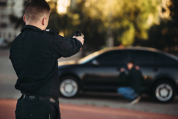 Politieagent met pistool in handen arresteert de auto dief. COP op het werk. Wet bescherming concept, professionele veiligheid controle - Foto, afbeelding