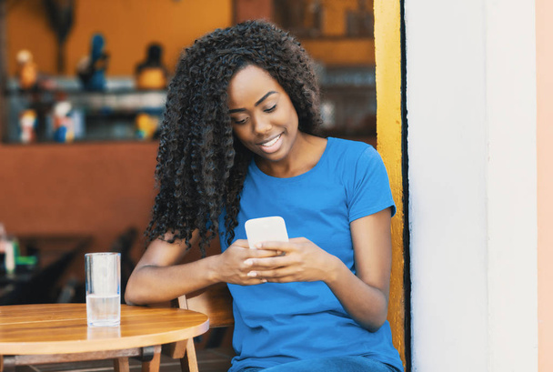 Laughing african american woman at bar texting message with mobile phone and using internet - Fotografie, Obrázek